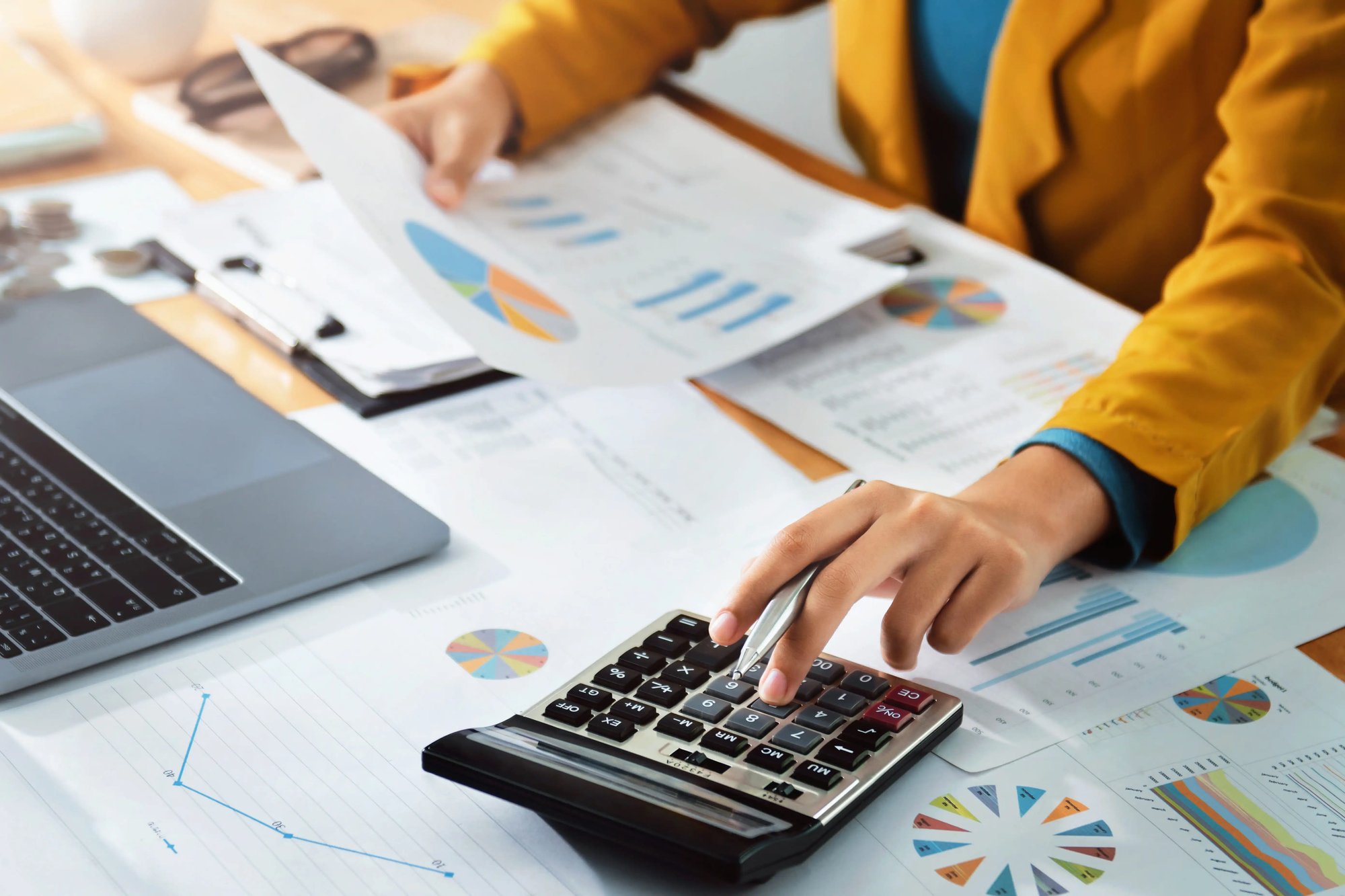 Person analyzing financial reports with a calculator and laptop, representing data analysis and financial management in the banking industry