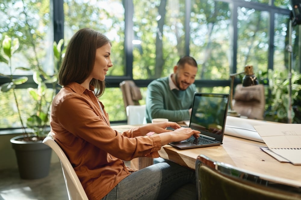 Professionals working with laptops in bright space – managing compliance with lifecycle tracking.